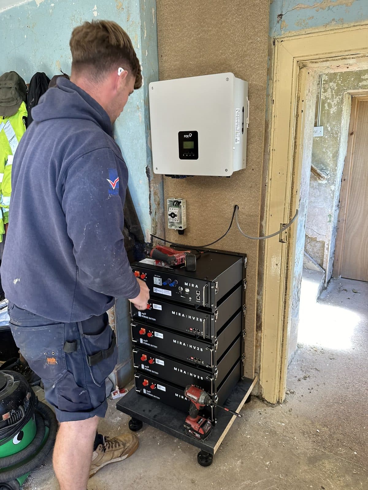 A GMC installer fitting a home battery beside an inverter